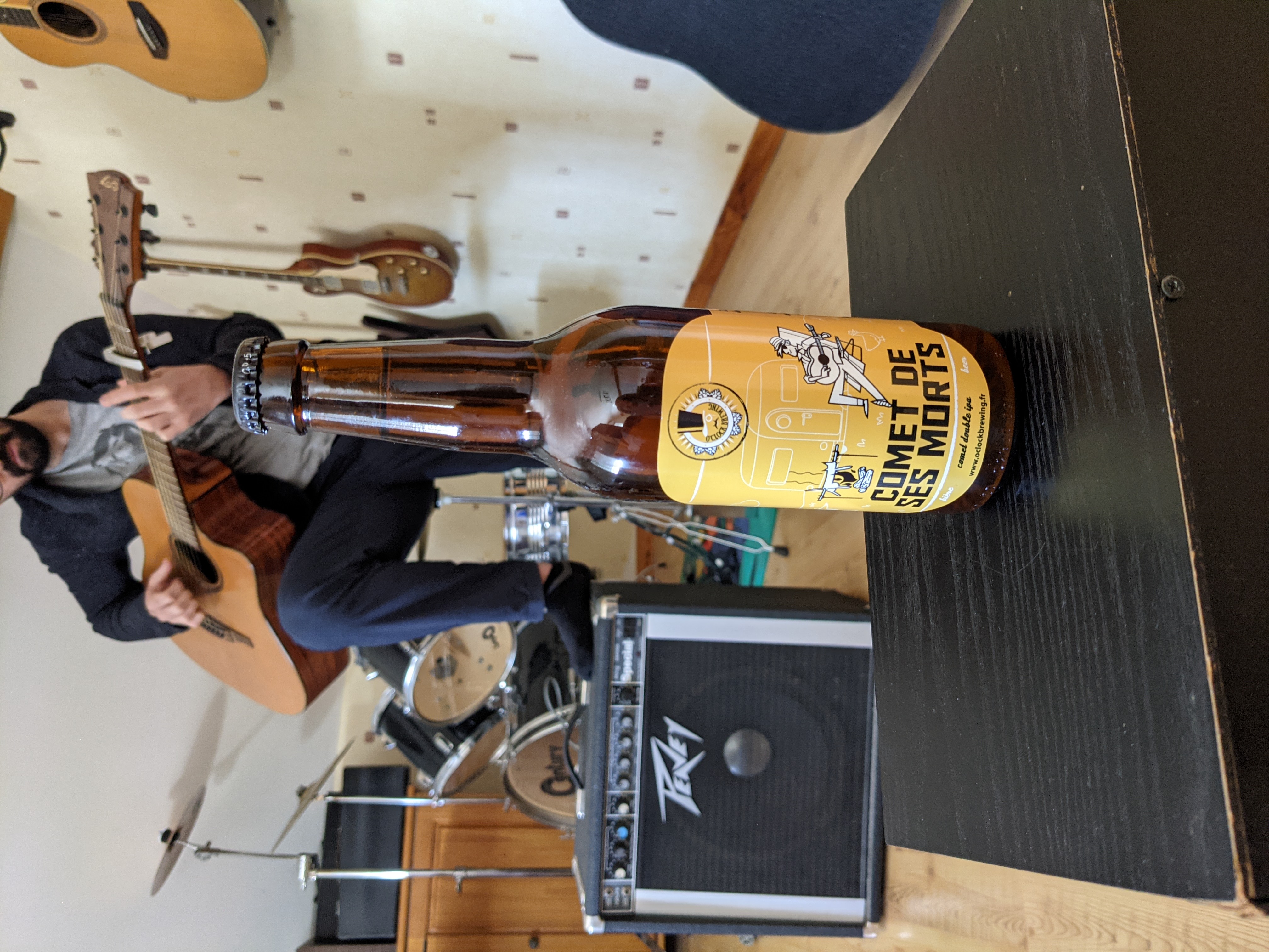Bouteille Comet de ses Morts (O'clock Brewing) avec un guitariste en arrière-plan